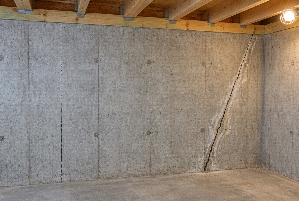 Illustration of a poured concrete basement wall with a single jagged crack running the full height of the wall, from the sill plate down to the floor, near the corner